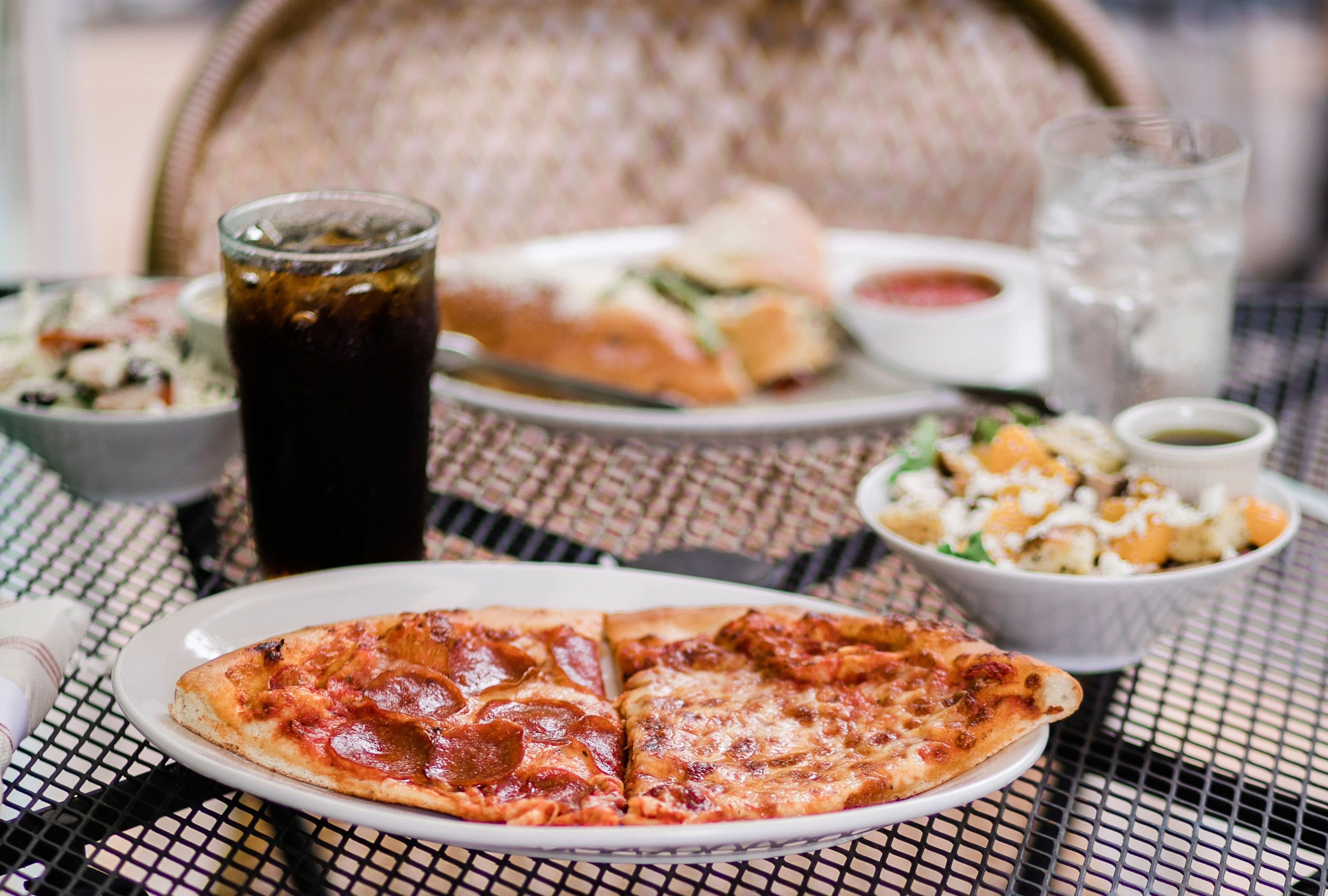 Photo of Outdoor table with pizza slices, salads, and drinks.