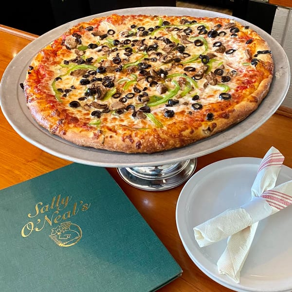 A large Sally O'Neal's pizza with black olives, green peppers, and mushrooms on a stand.