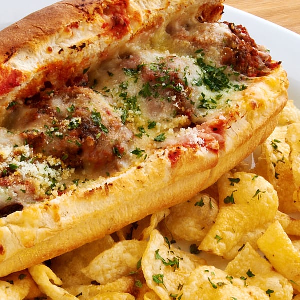 Meatball sub sandwich with melted cheese, marinara, and parsley, served with potato chips.