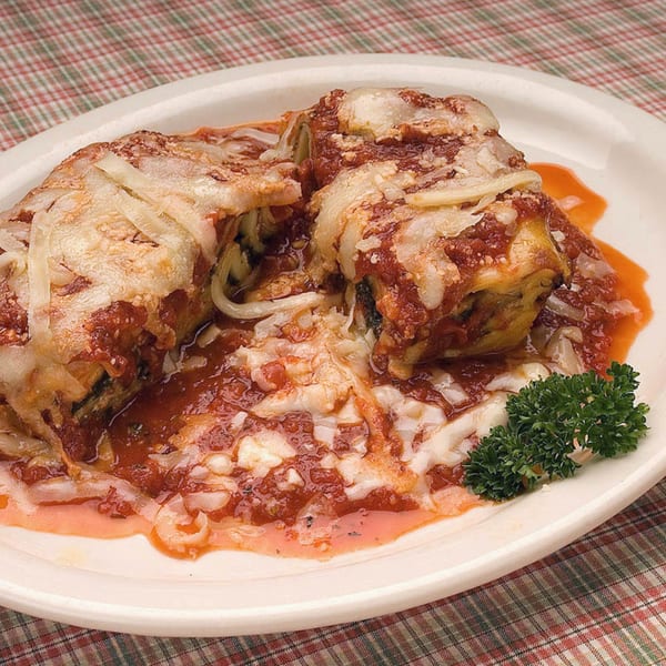 Three cheesy baked manicotti rolls covered in red sauce and parsley on a white plate.