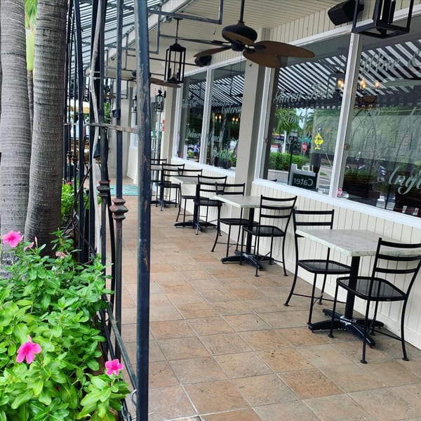 Outdoor patio seating at Sally O'Neal's Pizza Hotline with black tables and chairs, palm trees, and pink flowers.