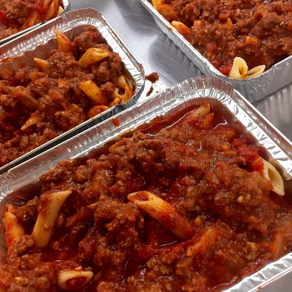 Several foil containers filled with penne pasta and rich meat sauce, ready for takeout.