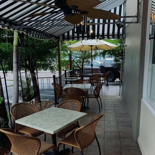 Outdoor patio seating area with wicker chairs, marble-top tables, and a striped awning at Sally O'Neal's.